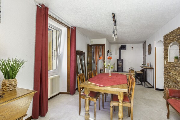 A dining area with a wooden table, red tablecloth, and chairs. There is a potted plant on a side table, a radiator, and a mirror on the wall.