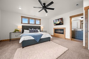 Une chambre à coucher comprenant un lit, des tables de chevet, un ventilateur de plafond, une télévision et une cheminée.