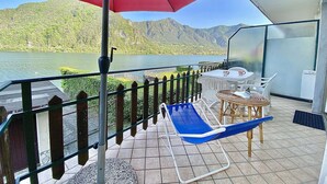 A balcony with a red umbrella, a table with chairs, and a blue lounge chair. - Directly on the lake with two bedrooms (Tre Capitelli)