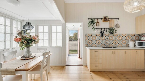 Une cuisine lumineuse avec des meubles en bois, un plan de travail blanc et un crédence décorée.
