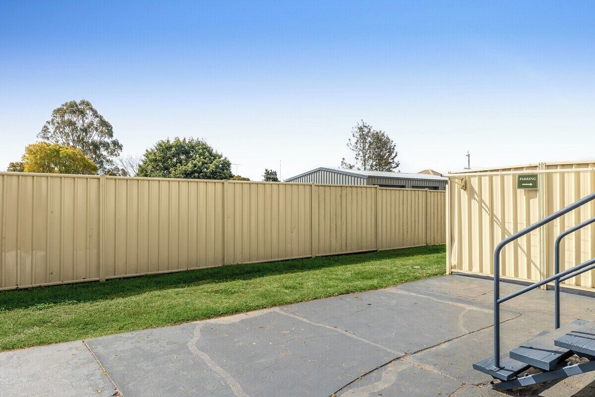 A fenced outdoor area with a paved walkway and a metal railing.