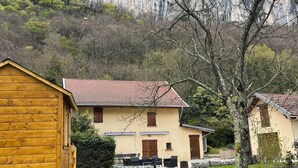 A wooden playhouse with a slide, a house with a red roof, and a mountain backdrop. - Gîte Champfleury (Chindrieux)