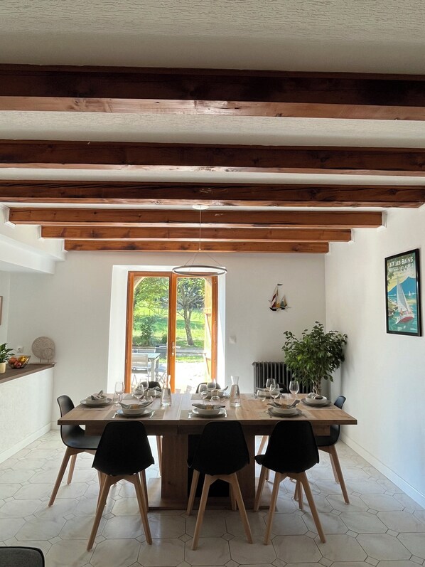 A dining area with a wooden table set for four, a large window with a view of greenery, and a radiator on the wall. - Gîte Champfleury (Chindrieux)