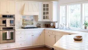 Una cocina con armarios blancos, estufa, microondas y un ventanal grande.