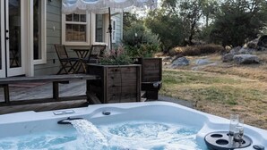 Un jacuzzi con dos vasos en una bandeja, una terraza de madera, una mesa con sillas y un área de patio techada.