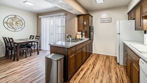 A compact kitchen with wooden cabinets, a dining area with a table and chairs, and a globe decoration on the wall. - Hoff Gardens 12 - 2BR 2BA - Downtown Lubbock (Lubbock)