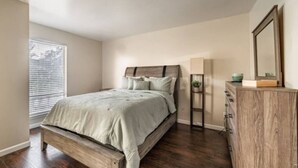 A bedroom with a bed, a dresser, a mirror, and a window with blinds. - Hoff Gardens 10 - 2BR 2BA - Downtown Lubbock (Lubbock)