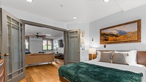 Ein Schlafzimmer mit einem großen Bett, einem Gemälde einer Berglandschaft und Blick auf einen Garten durch eine offene Tür.