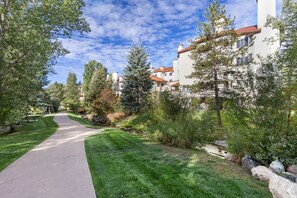 A residential area with a paved walkway, green lawns, and trees. - 2 King Suites • Walk to Gondola & Base • Pool & Hot Tub • Spacious 1848 sq ft (Steamboat Springs)