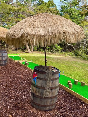 Een houten vat met een netdeksel, een kleine papegaai beeldje en een minigolfbaan met een groene mat en houten hindernissen.