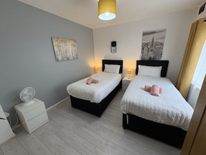 Une chambre d’hôtel avec deux lits, une table de chevet avec une lampe, une horloge murale et un tableau représentant un paysage urbain.
