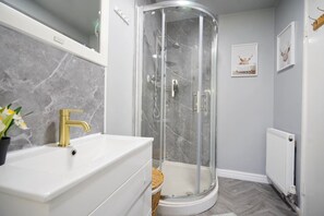 Un bany modern amb un moble de bany blanc, una cabina de dutxa de vidre i un radiador.