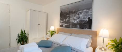 Ein ordentlich eingerichtetes Schlafzimmer mit Bett, Nachttischen, einem Kleiderschrank und einem Stadtbild an der Wand.
