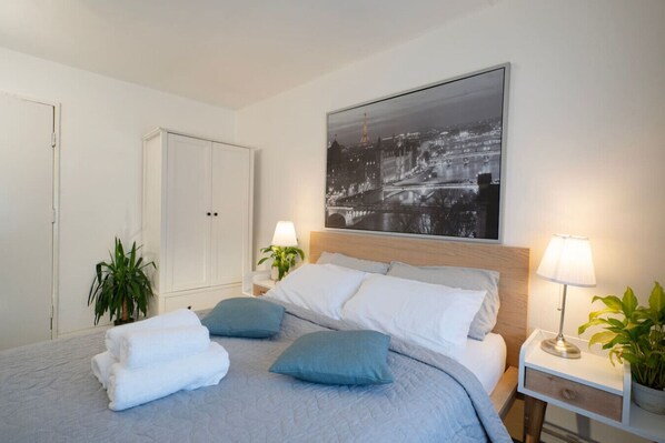 Een netjes ingerichte slaapkamer met een bed, nachtkastjes, een kledingkast en een stadsgezichtschilderij aan de muur.