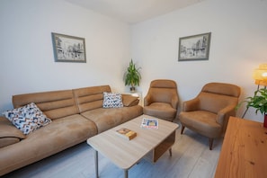 Un salon avec un canapé marron, deux fauteuils, une table basse et deux tableaux encadrés accrochés aux murs.