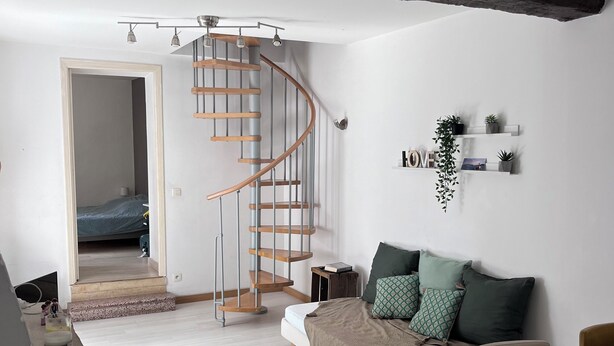 Ein modernes Wohnzimmer mit Wendeltreppe, einer Couch mit Kissen, einem Couchtisch und einem Bücherregal mit Pflanzen.