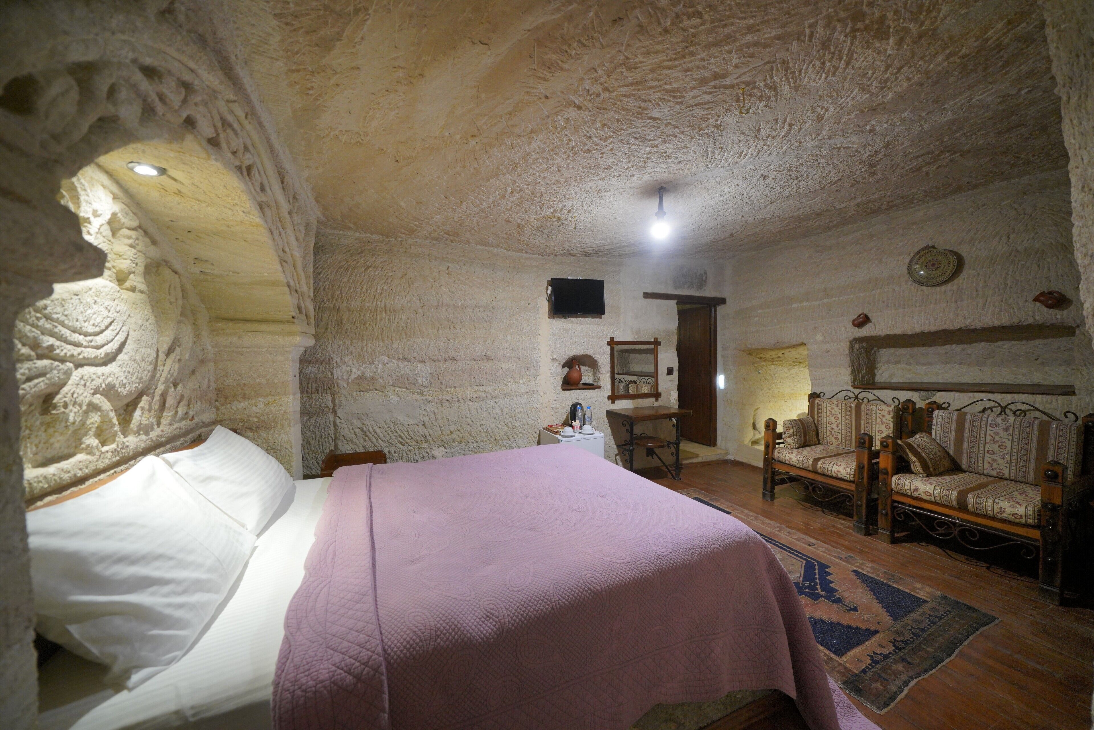 A room with a bed, a wooden chair, a small table, and a stone wall with carvings.