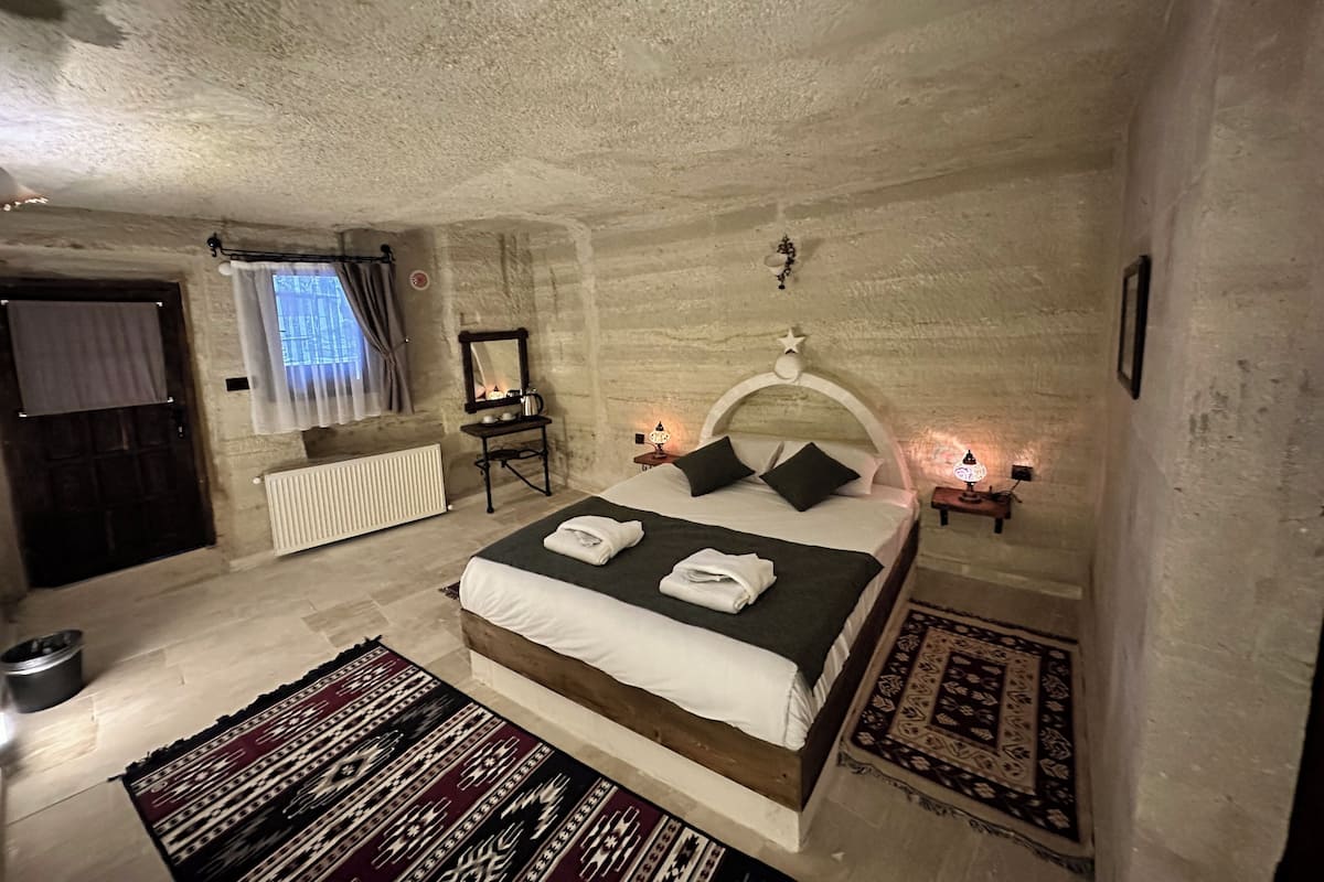 A bedroom with a bed, two bedside tables with lamps, a radiator, a window with curtains, a mirror, and a wall-mounted star decoration.