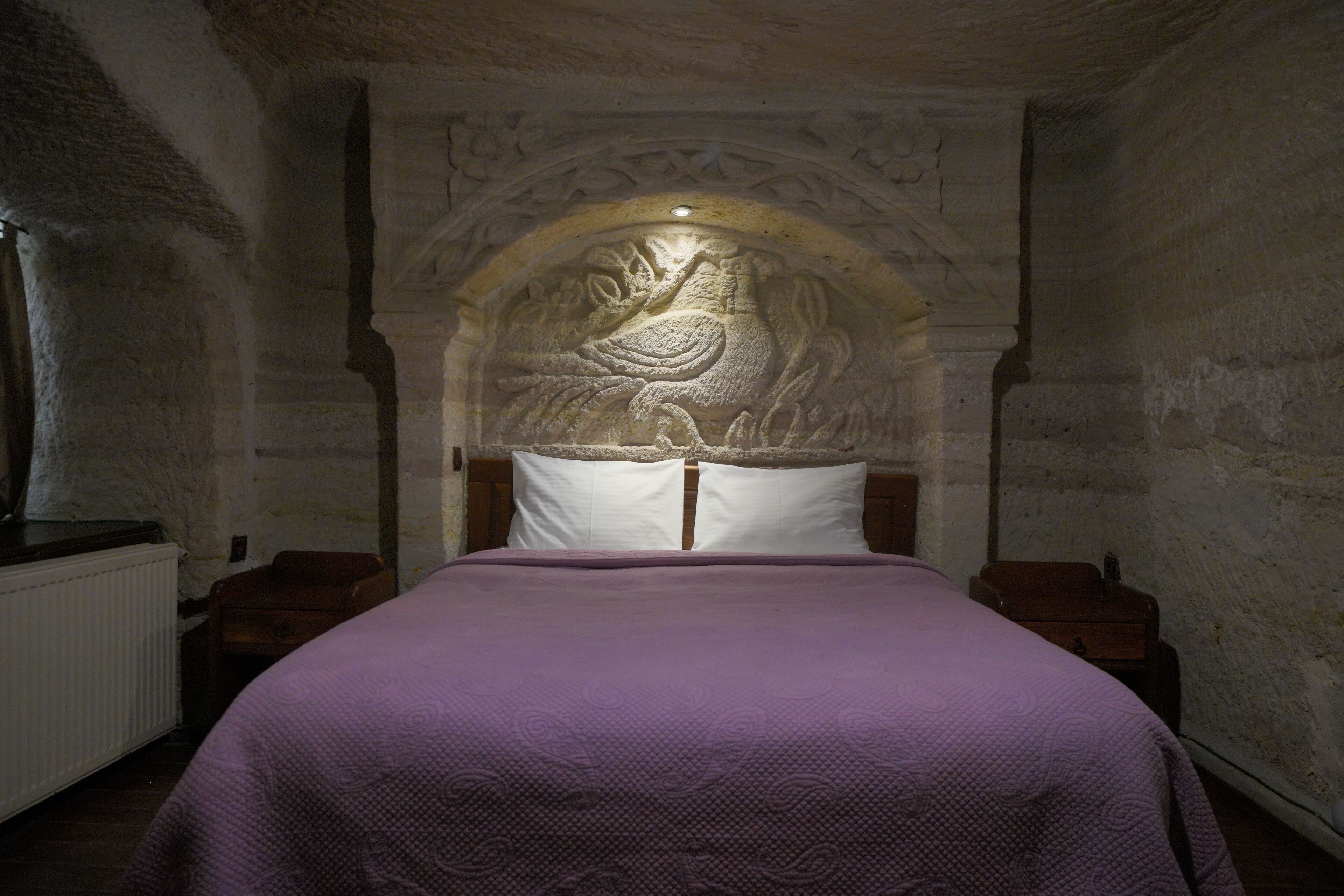 A bedroom with a stone-carved headboard, a purple bedspread, and a white pillow.