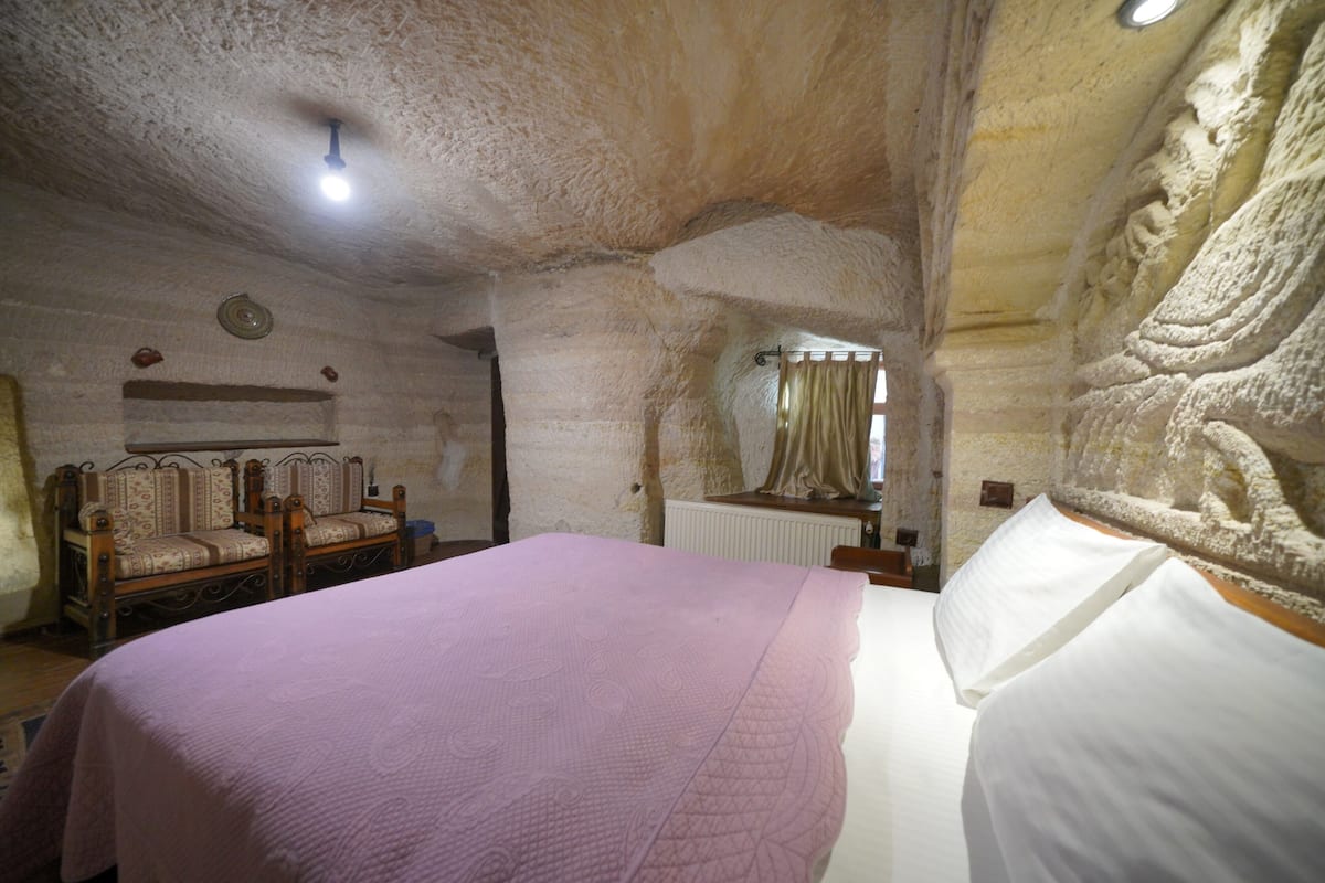 A room with a bed, two chairs, a radiator, and a stone wall with carvings.