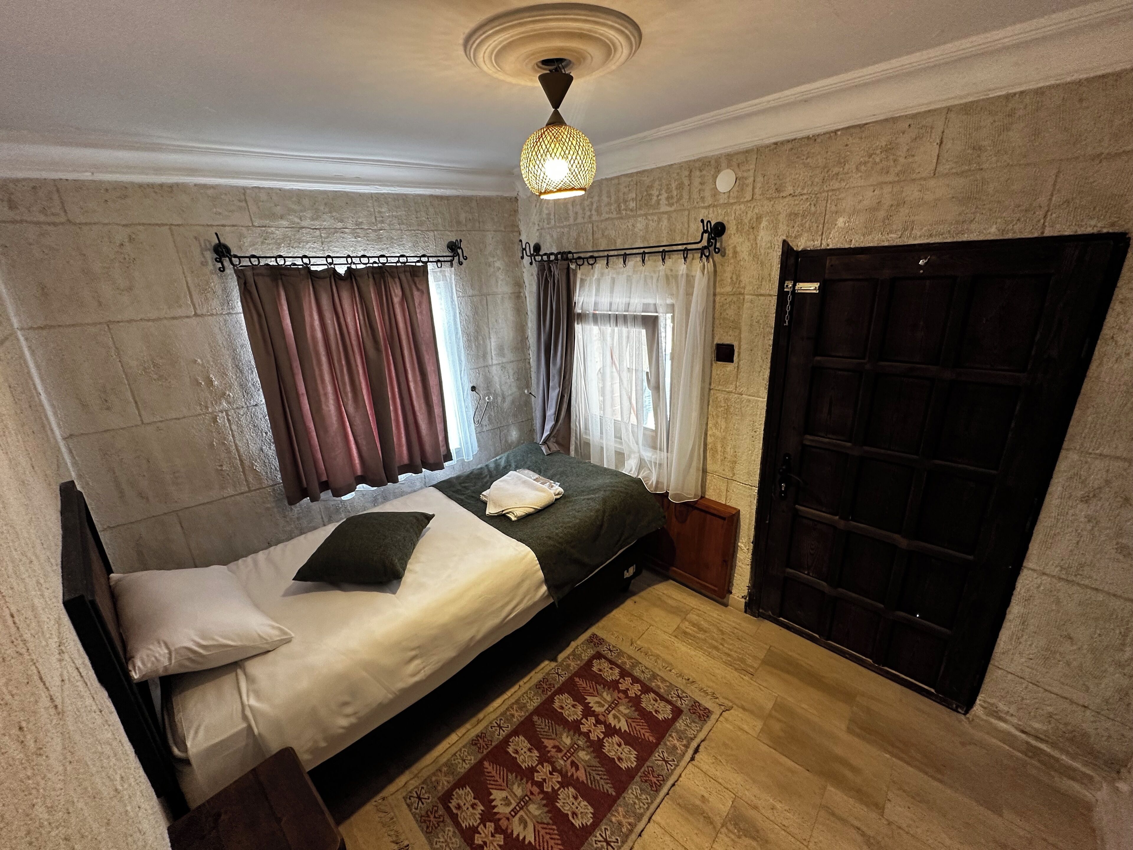 A bedroom with a bed, a window with curtains, a door, and a patterned rug.