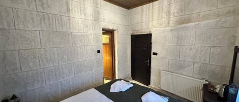 A room with a bed, a wooden door, a radiator, and a small table with a kettle.