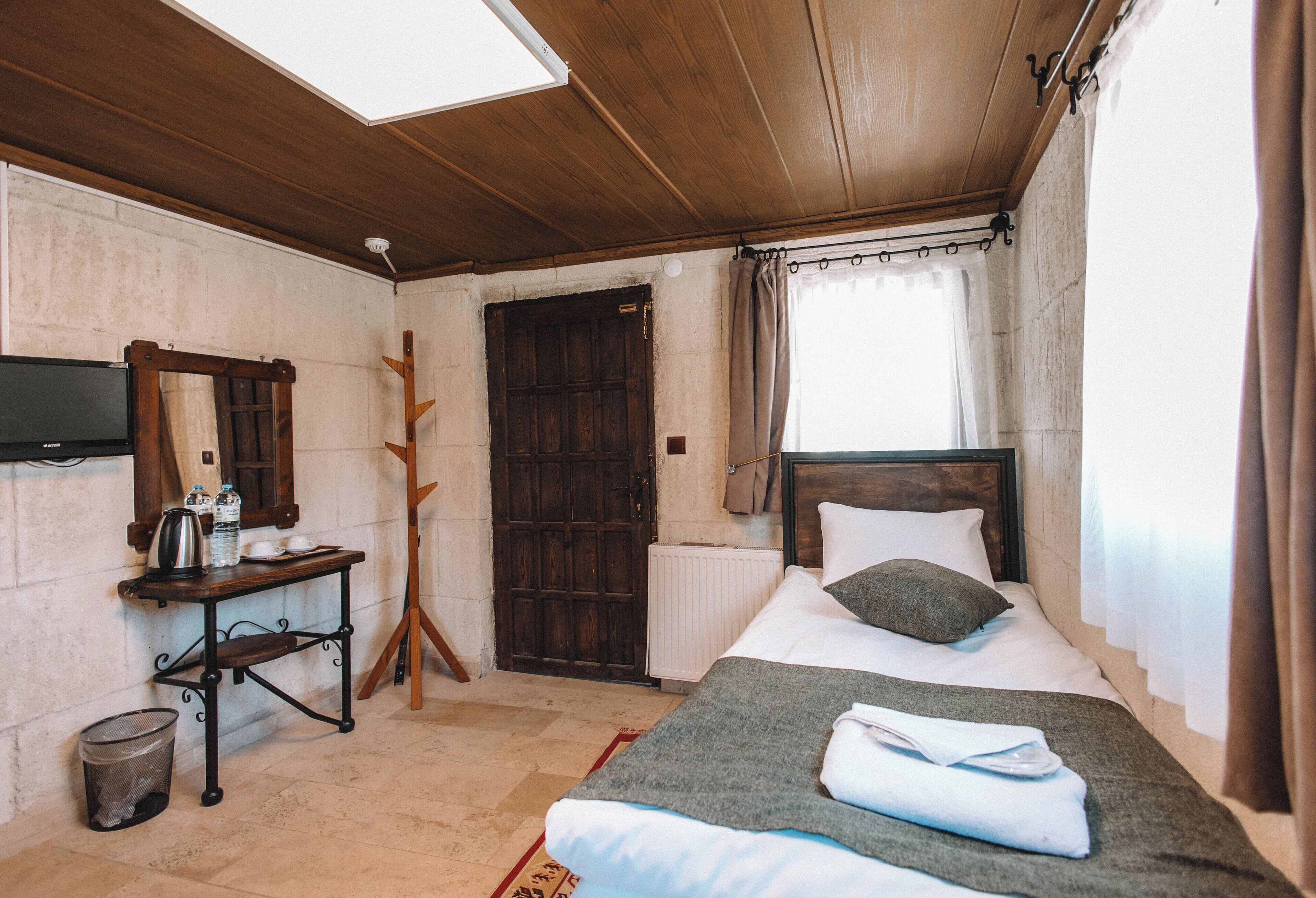 Een kamer met een houten plafond, een bed met kussens, een tafel met waterkoker, een spiegel en een deur.