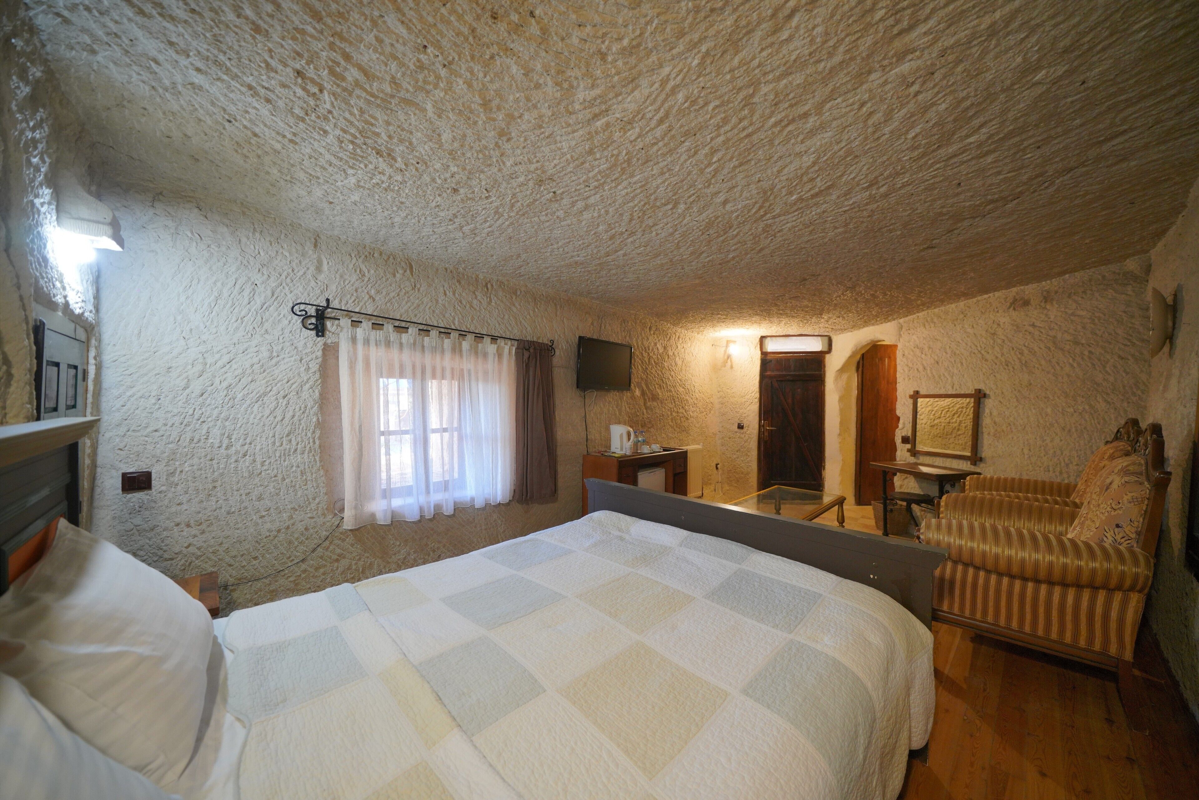 A bedroom with a large bed, a bedside table, a chair, a television, and a mirror.