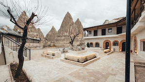 A courtyard with stone flooring, a tree, and a building with arched windows. - TURAN Cappadocia Cave (Nevsehir)
