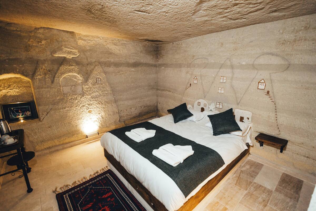 A bedroom with a stone wall, a bed with white linens, a bedside table, and a nightstand.