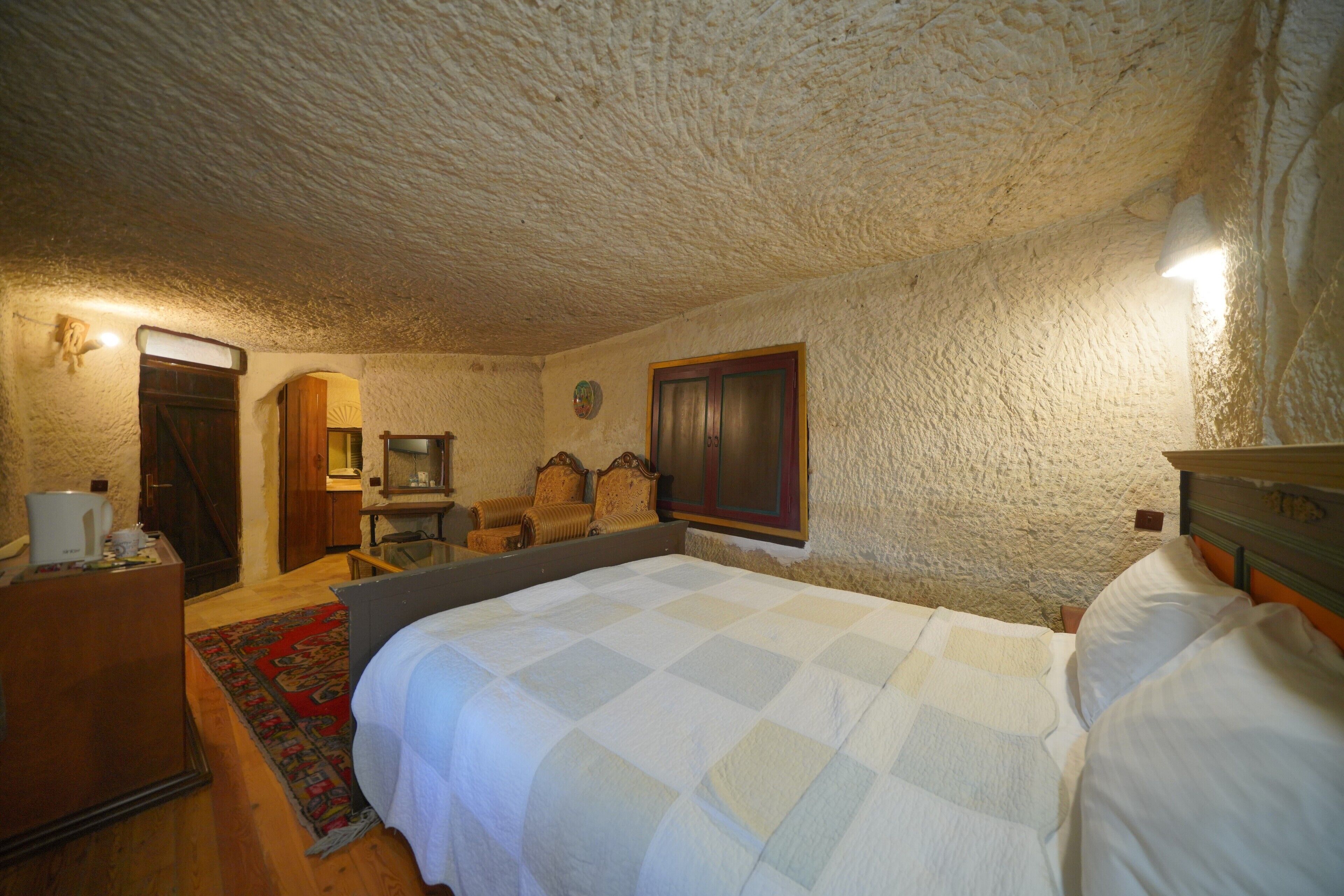 A bedroom with a large bed, a wooden dresser, a desk with a chair, a small table, and a mirror.