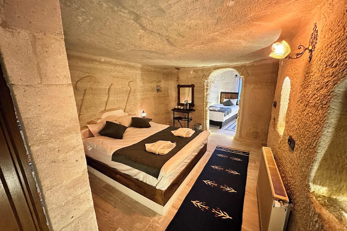 A stone-walled bedroom with a bed, a nightstand, and a hallway leading to another room.