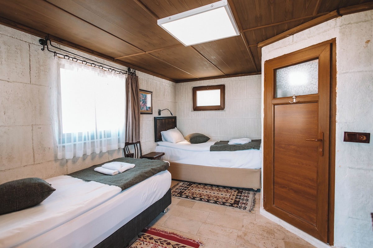 A room with two beds, a wooden door, and a window with curtains.