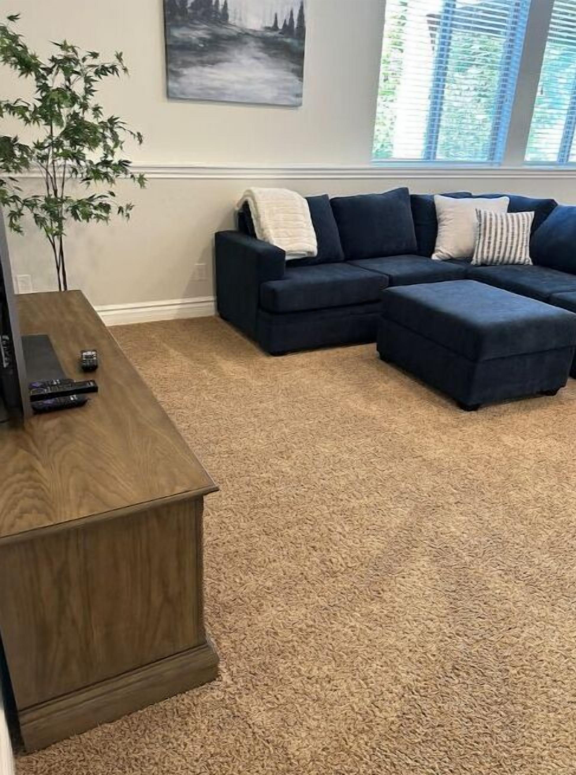 A living room with a dark blue sectional sofa, a wooden coffee table, and a large window with blinds.