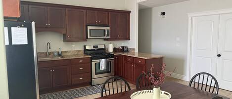 A modern kitchen with dark wooden cabinets, stainless steel appliances, and a dining area with a wooden table and chairs.