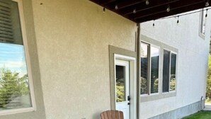 A covered patio with two Adirondack chairs and a small table, adjacent to a building with a door and windows.
