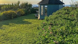 Un petit bâtiment d’un seul étage, doté d’un toit sombre et d’une porte en verre, entouré d’une pelouse verdoyante et de buissons en fleurs.