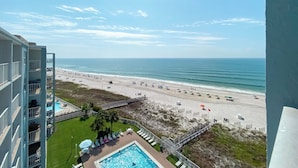 Un hotel de gran altura con zona de piscina, vistas a la playa y una playa de arena con sombrillas.