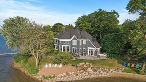 A large, two-story house with a wrap-around porch, situated on a lakeside property. - The Luxury Lake Minnetonka Home, Hot Tub, Captain Services, 4 Bedrooms, on lake (Shorewood)