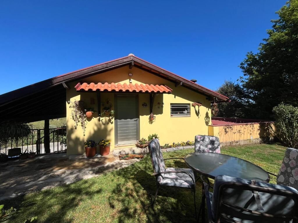 Una casa amarilla con techo rojo, un patio con sillas y una mesa.