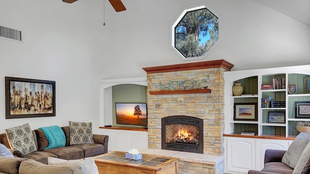 A living room with a stone fireplace, a television, and a bookshelf. - Oriole (Flagstaff)