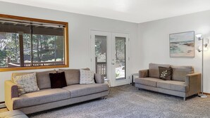 A living room with two sofas, a coffee table, and a large window with a view of trees. - Oriole (Flagstaff)