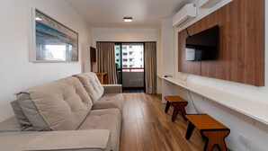 A modern living room with a sofa, wooden flooring, a mounted TV, and a view of a building through the window. - Metropolitan Flats (Curitiba)