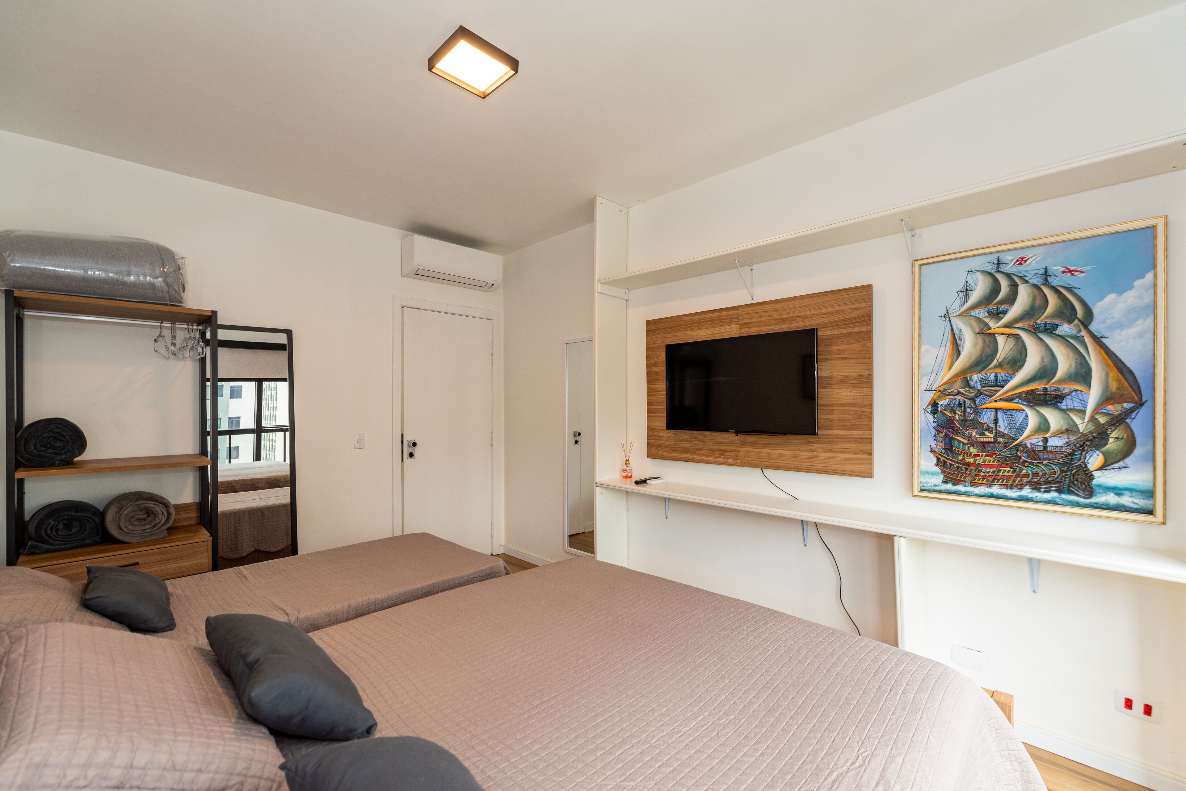 A bedroom with two beds, a TV mounted on the wall, and a painting of a ship.