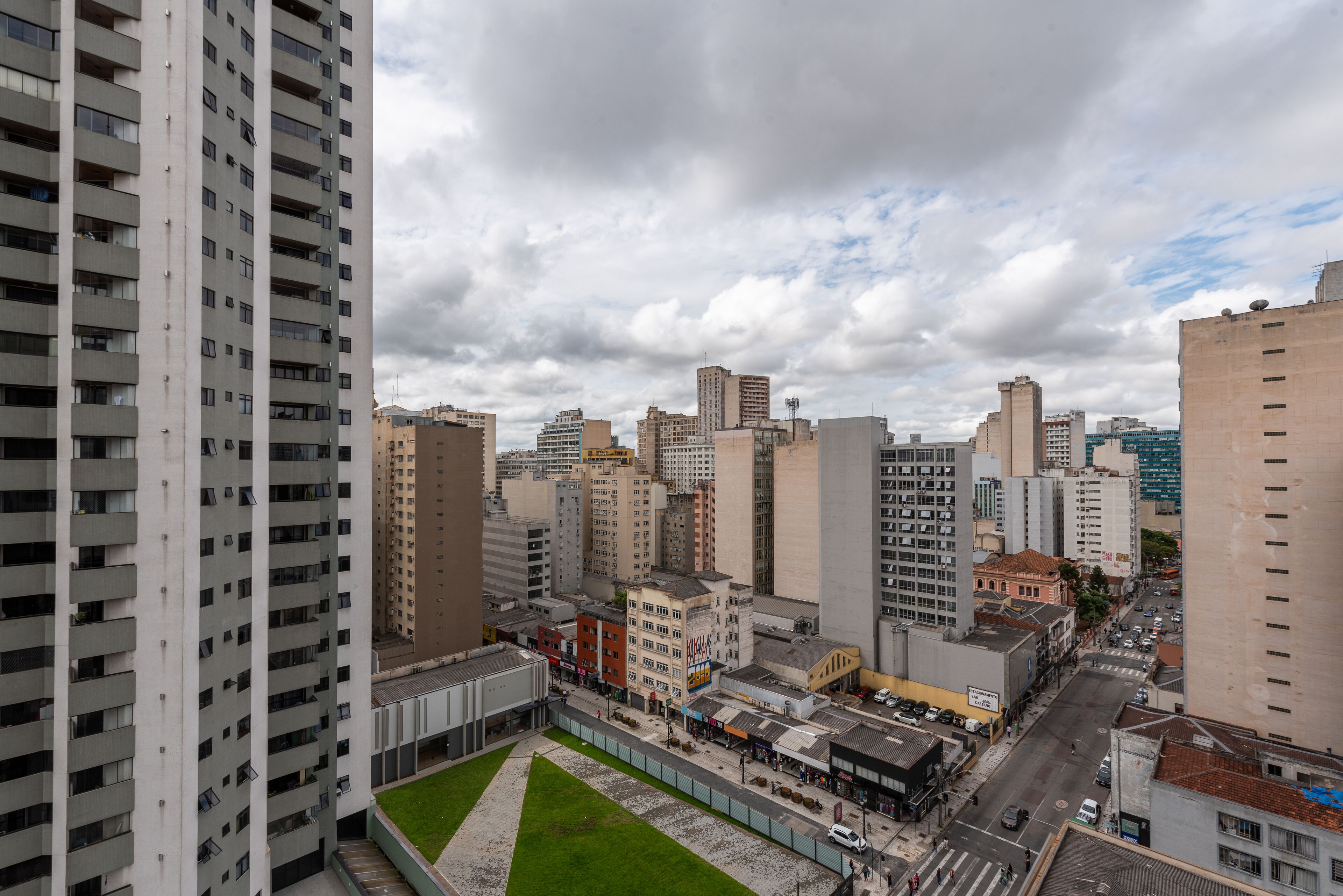 A high-rise building with multiple floors and balconies, surrounded by other buildings and a street with cars and pedestrians.