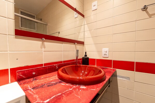 Un baño con un lavamanos rojo, azulejos blancos y una franja roja decorativa.