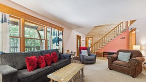 Un salon avec un canapé gris, des coussins rouges, une table basse en bois et un fauteuil marron.