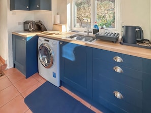 Une cuisine compacte équipée d’un lave-linge, d’un évier et d’une fenêtre donnant sur un espace verdoyant.