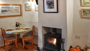 A dining area with a table set for two, a fireplace, and framed pictures on the wall.