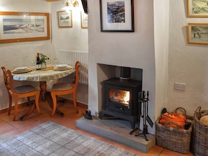 A dining area with a table set for two, a fireplace, and framed pictures on the wall. - 1 bedroom accommodation in Ennerdale (Ennerdale)